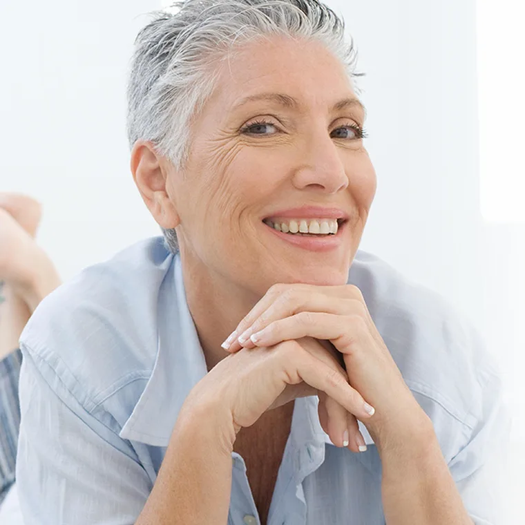 A smiling patient resting her chin on her hands in a bright room